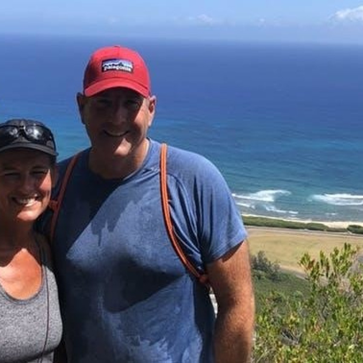 Two people posing on a hilltop with an ocean view in the background.