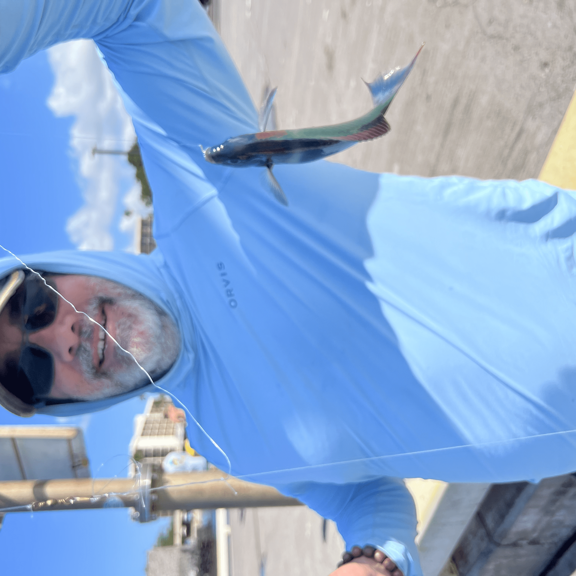 Person in a blue hoodie holds up a small fish on a line outdoors.